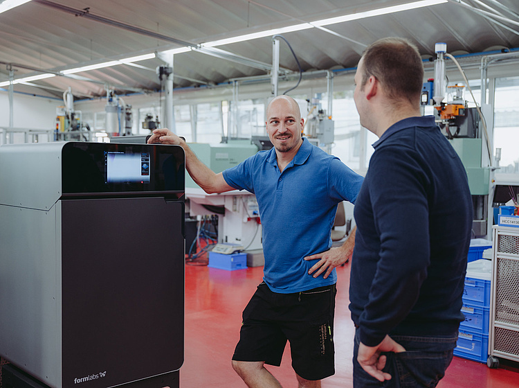 2 Mitarbeiter stehen vor einem 3D-Drucker bei Simply3D